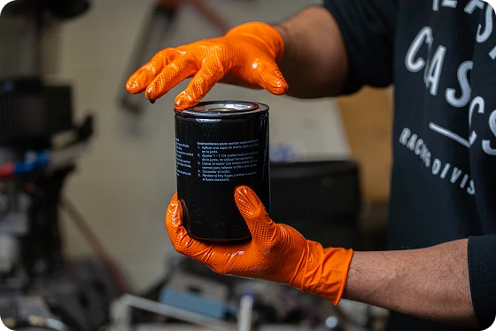 Mechanic wearing high-visibility 8 mil orange iGrip nitrile gloves while handling an automotive oil filter.