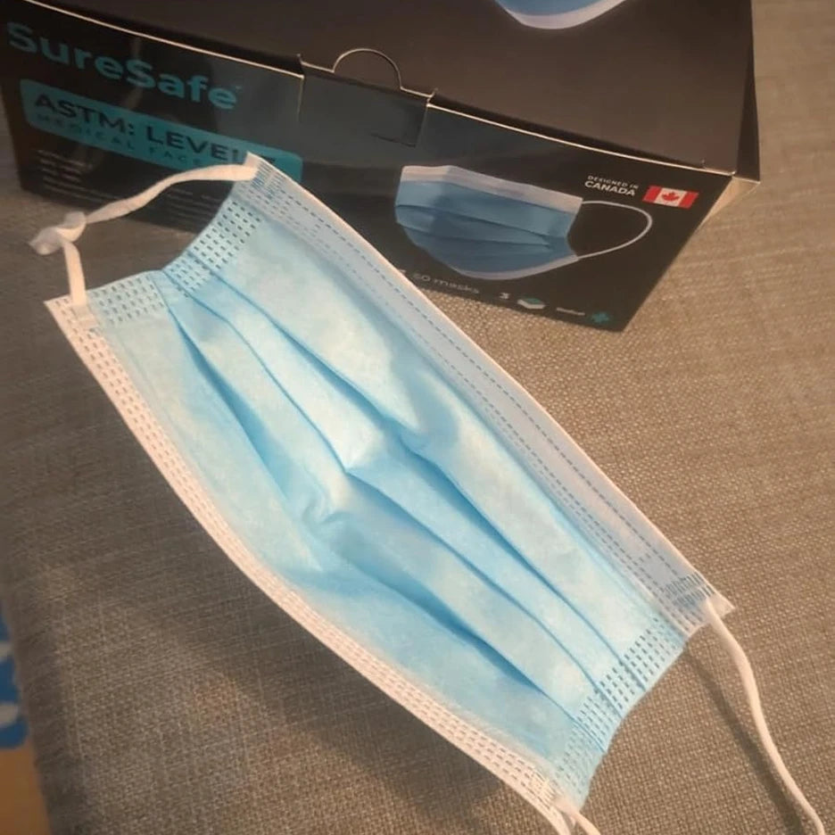 Close-up of SureSafe blue 3-ply surgical mask featuring a soft inner layer, adjustable nose bridge, and elastic ear loops.